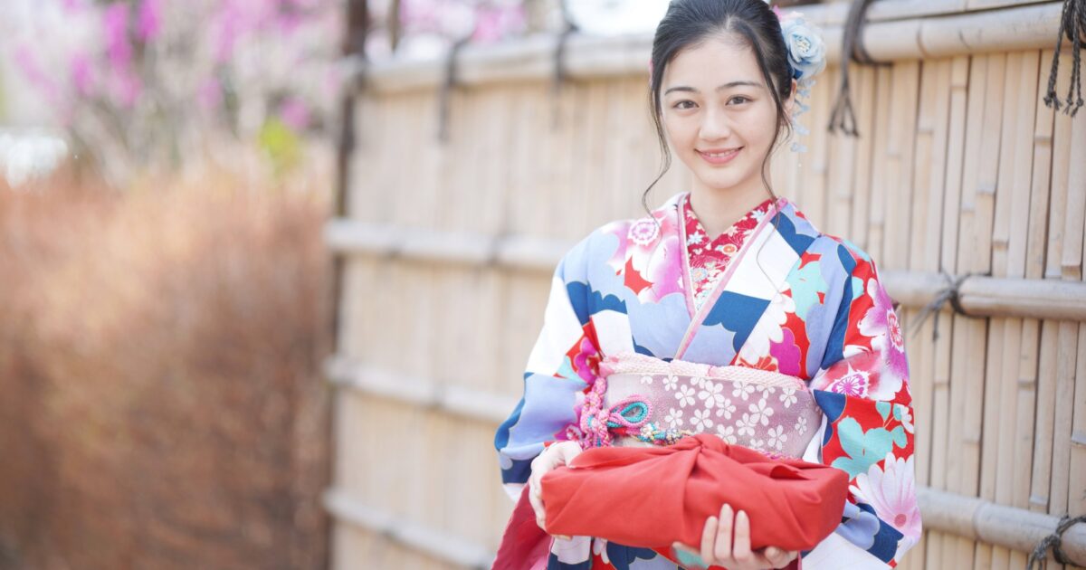 伝統的な竹垣の前で着物姿の女性が風呂敷を持つ様子