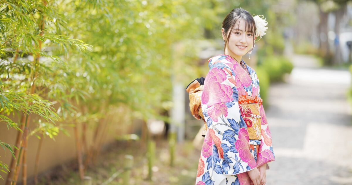 華やかな着物を着た女性が竹林の小道で微笑む様子