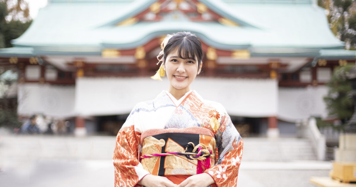 神社の前で振袖姿の女性が笑顔を見せる様子