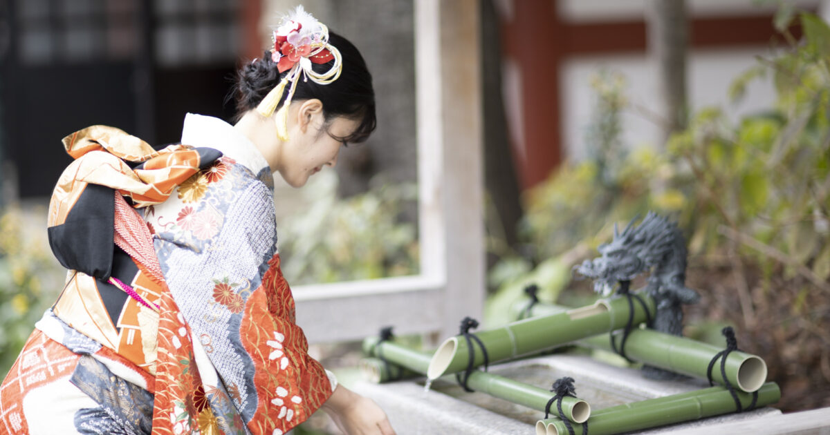 神社の手水舎で手を清める振袖姿の女性