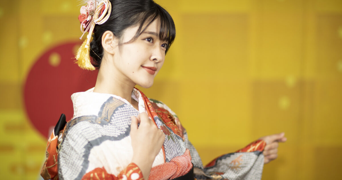 華やかな振袖を着た女性が金屏風の前で微笑む様子