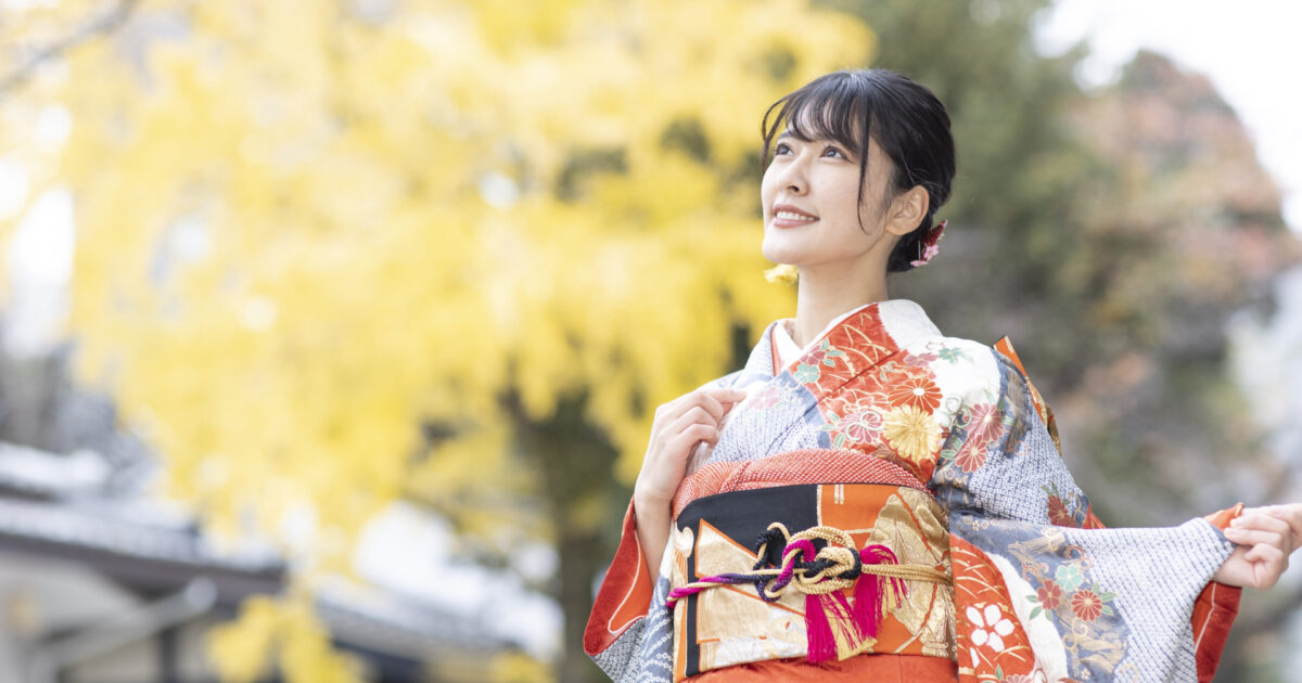 秋の銀杏並木で振袖姿の女性が空を見上げる様子
