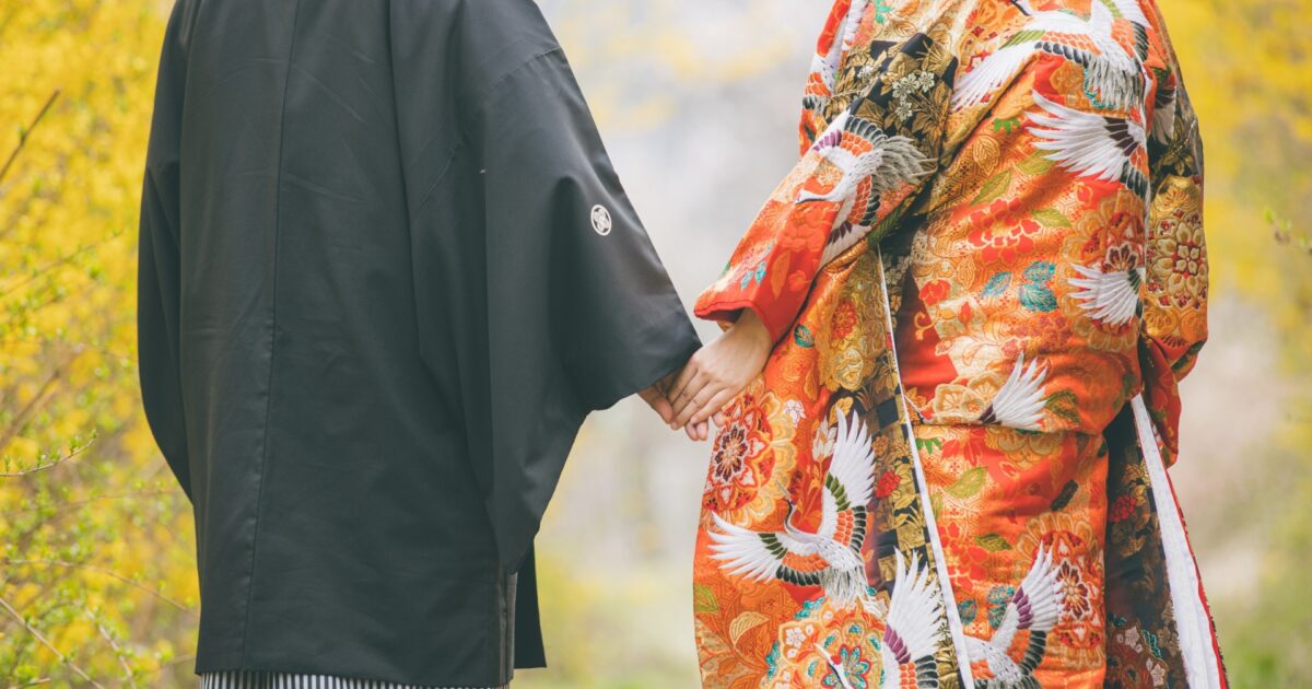 和装の男女が紅葉の中で手をつないで歩く後ろ姿