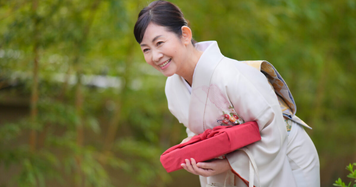 着物姿の女性が笑顔で風呂敷を持ってお辞儀する様子