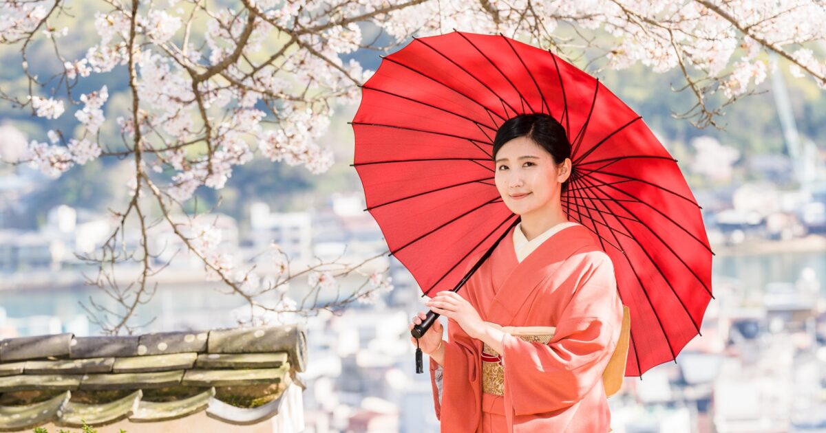 桜の下で赤い和傘を持つ着物姿の女性