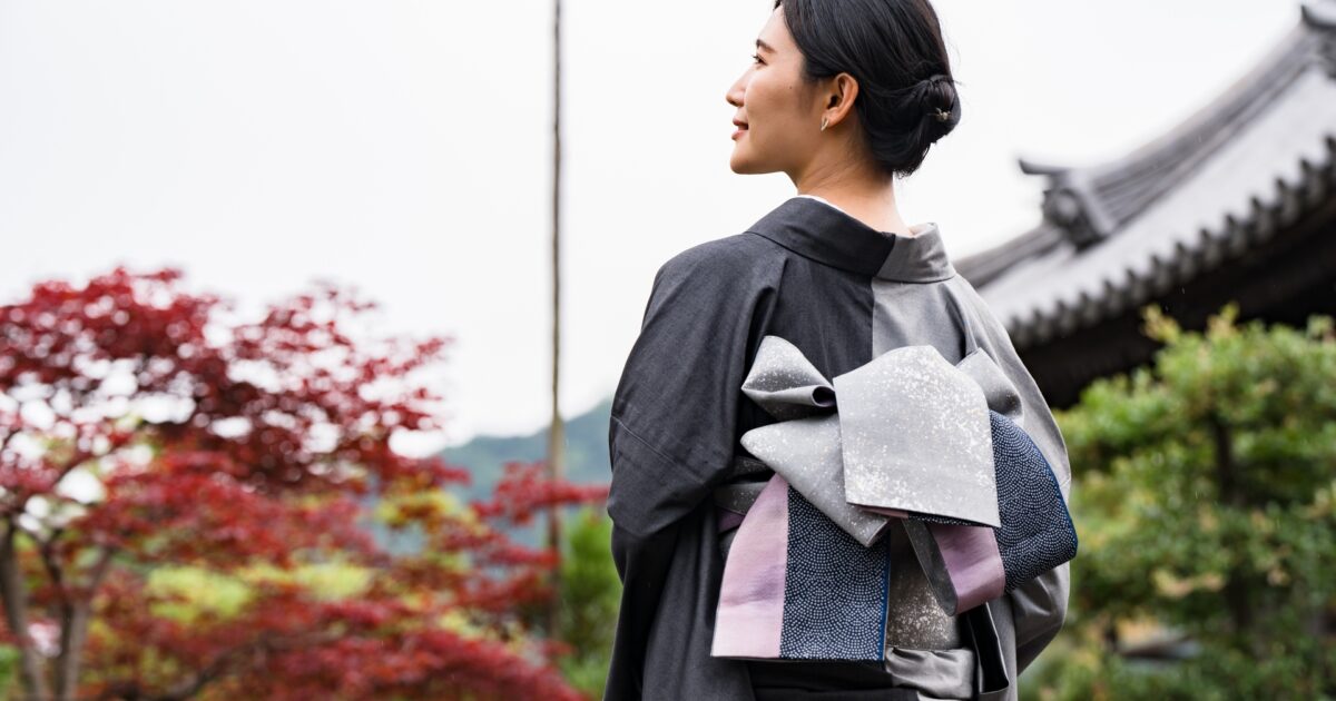 紅葉と寺院を背景にシックな着物を着た女性の後ろ姿