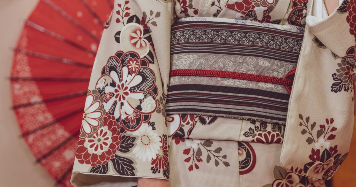 和傘の前で手を揃える花柄の着物を着た女性のアップ