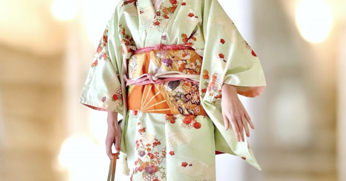 若草色の訪問着と華やかな帯を着た女性の全身コーディネート
