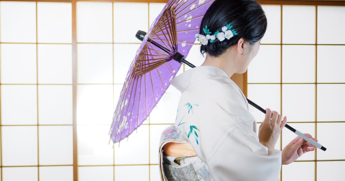 障子の前で紫の和傘を持つ着物姿の女性の後ろ姿