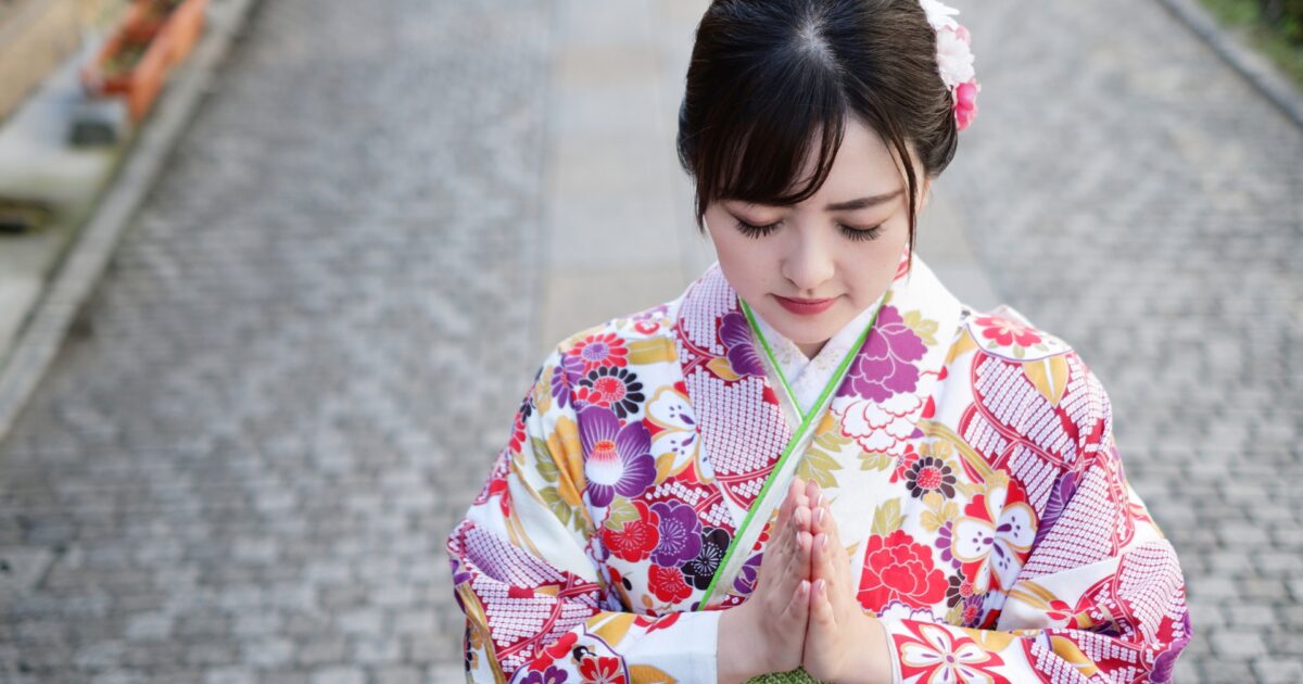 石畳の道で手を合わせる華やかな振袖姿の女性